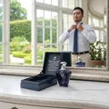 Premium fragrance Turathi Blue Afnan – Man adjusting his tie in front of a mirror with a blue perfume bottle and packaging on a table.