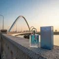 Supremacy In Heaven perfume bottle placed on Putrajaya bridge rail, soft blue sunset, gentle wind, elegant masculine tones, cinematic Malaysian atmosphere.