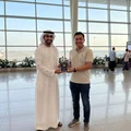 Two men standing in an airport terminal, one holding a trophy