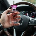 Hand holding a perfume bottle with Arabic text in front of a car dashboard.