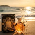 Perfume bottle broken, amber glow emerging; Langkawi beach at sunset Malaysia — clear bottle and box, cinematic lighting