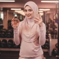 Hijabi woman holding Club De Nuit Woman by Armaf near gym mirror