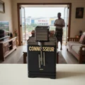 Black coffee grinder with 'CONNOISSEUR' branding on a table in a living room