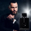 Man in a suit with a beard holding a watch, next to an Armaf 'club de nuit intense man' perfume bottle