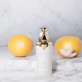 White skincare bottle with gold cap on a marble surface with two yellow fruits