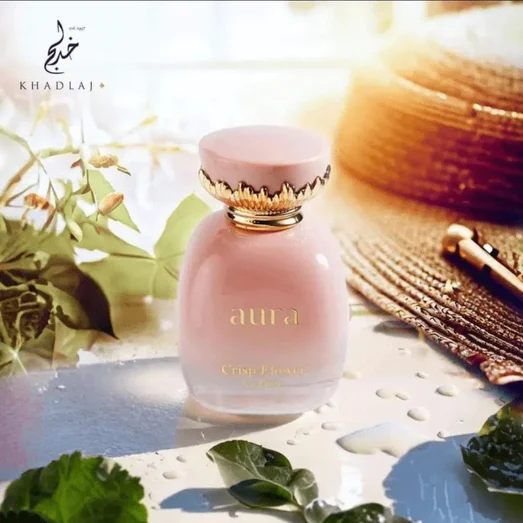 Perfume bottle labeled 'aura' by Khadlaj with a sun hat and greenery in the background