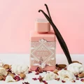 Pink perfume bottle with vanilla beans and flowers on a pink background