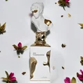 Perfume bottle labeled 'Her Confession' with decorative bust on a light background with flowers