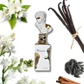 Perfume bottle labeled 'Her Confession' with vanilla beans, flowers, and cinnamon sticks on a white background