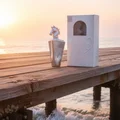 Lattafa Maahir Bottle & box placed on weathered teak pier by the sea at golden hour; ocean waves gently lapping; salt mist visible; sunrise/early morning light