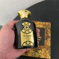 Hand holding a black and gold perfume bottle labeled 'Nasheet Lattafa' with a blurred background