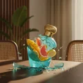 Lattafa Opulent Dubai 100 ml –Decorative bottle with fruit design on a table with chairs and a plant in the background