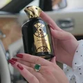 Hand holding a black and gold bottle with 'Nasheet Lattafa' branding, inside a car