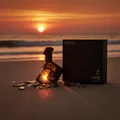 Perfume bottle broken, amber glow emerging; Langkawi beach at sunset — clear bottle and box, cinematic lighting.