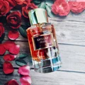 Perfume bottle labeled 'Exclusif Rose' surrounded by red roses and petals on a wooden surface