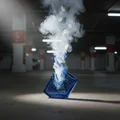 Blue smoke device labeled 'LUXE' emitting smoke in a dark indoor setting