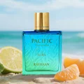 Blue perfume bottle with gold cap labeled 'Pacific Aura Rayhaan' on a beach with fruits.